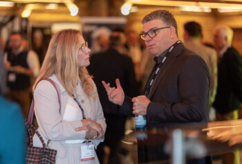 Eine Frau und ein Mann mit Namensschildern unterhalten sich auf einer Konferenz oder einem Networking-Event, wobei die anderen Teilnehmer im Hintergrund verschwimmen.