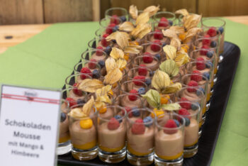 Reihen von kleinen Gl&auml;sern, gef&uuml;llt mit Schokoladenmousse, Mangop&uuml;ree, Himbeeren, Blaubeeren und gekr&ouml;nt mit einer dekorativen Schalen-Kirsche, fein s&auml;uberlich auf einem Tablett angeordnet. Auf einem Schild steht 