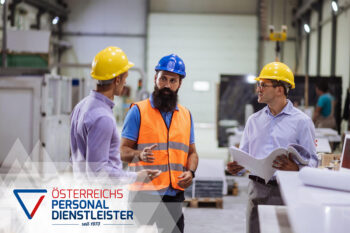 Drei M&auml;nner mit Schutzhelmen und Sicherheitsausr&uuml;stung stehen in einer Fabrik und diskutieren. Zwei halten Dokumente in der Hand. Auf dem Logo steht: 